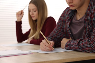 Photo of Students taking exam at wooden table indoors, selective focus