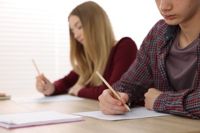 Photo of Students taking exam at wooden table indoors, selective focus