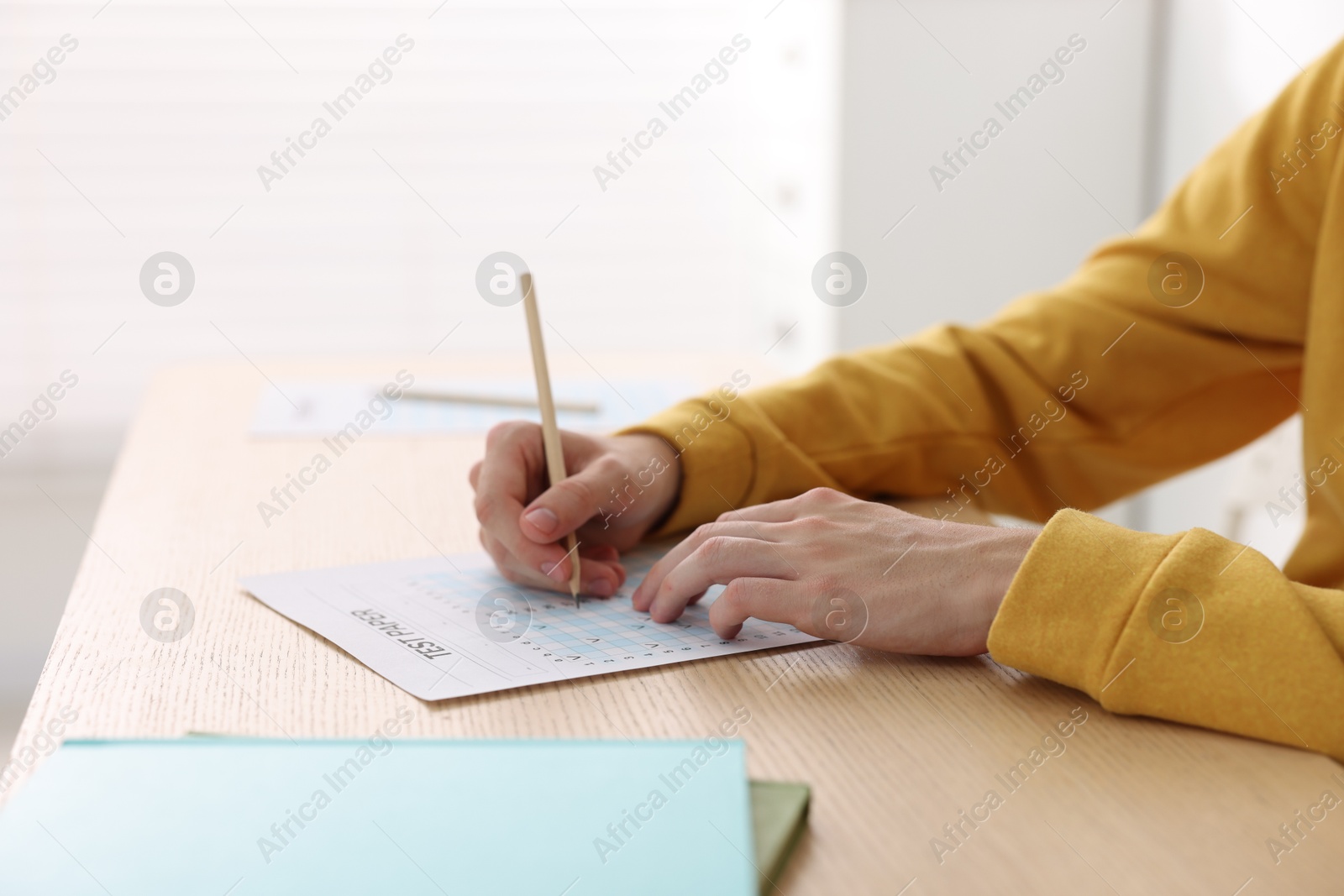 Photo of Student taking exam at wooden table indoors, closeup