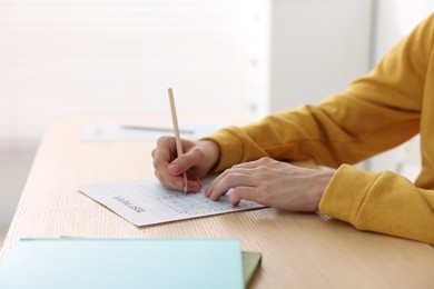 Photo of Student taking exam at wooden table indoors, closeup