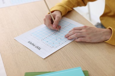 Photo of Student taking exam at wooden table indoors, closeup