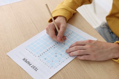 Photo of Student taking exam at wooden table indoors, closeup