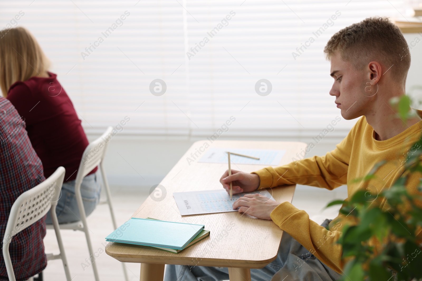 Photo of Students taking exam at wooden table indoors