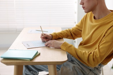 Photo of Student filling out answer sheet at wooden table indoors, closeup. Taking exam