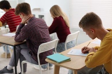 Photo of Students taking exam at wooden table indoors, selective focus