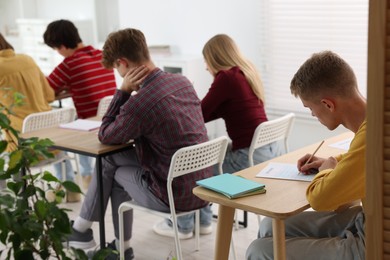 Photo of Students taking exam at wooden table indoors, selective focus
