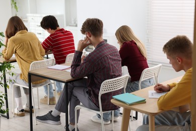 Photo of Students taking exam at wooden table indoors