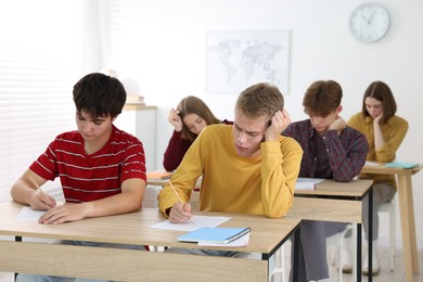 Photo of Students taking exam at wooden table indoors