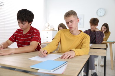 Photo of Students taking exam at wooden table indoors