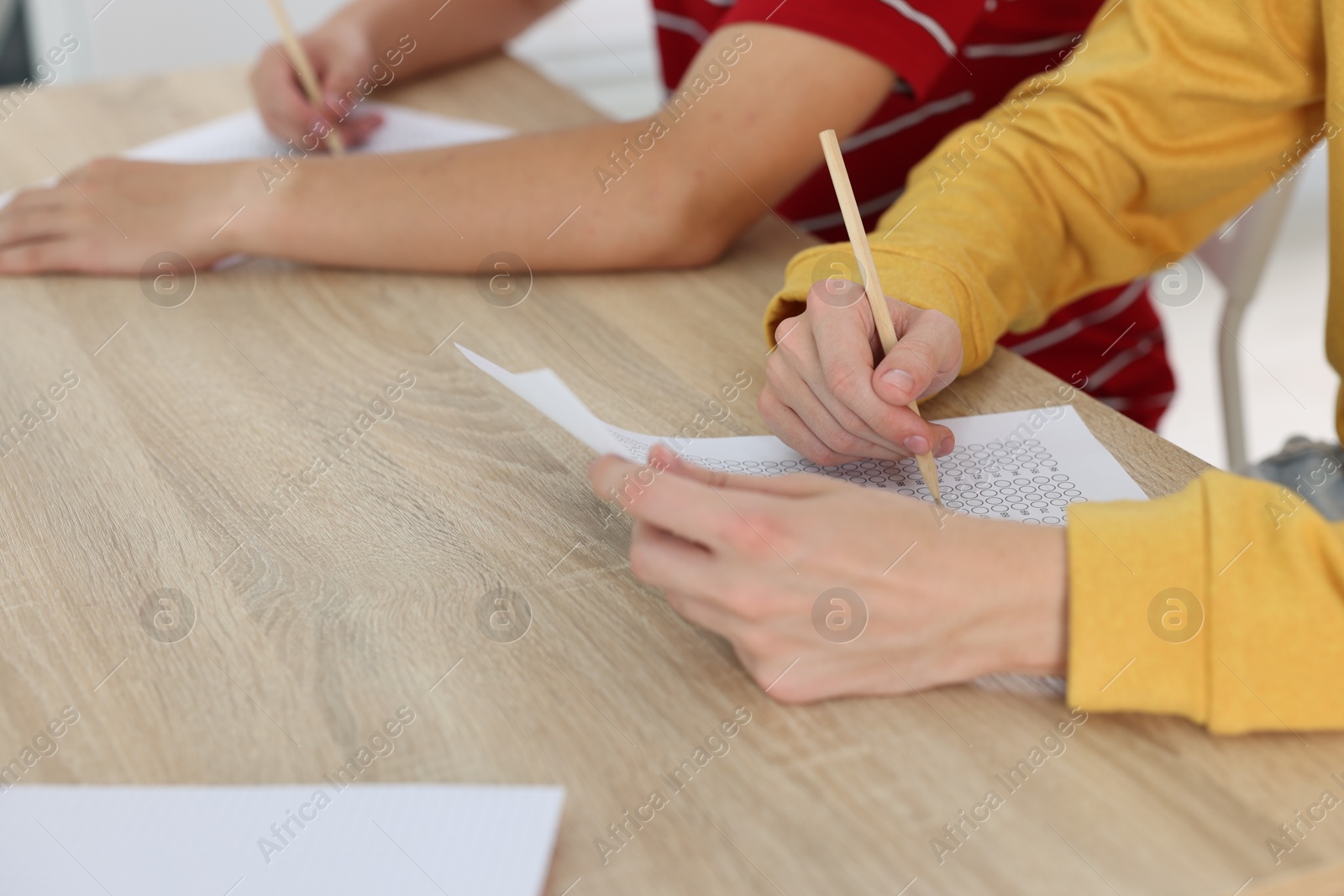 Photo of Students filling out answer sheet at wooden table indoors, closeup. Taking exam