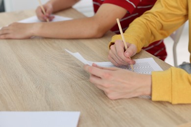 Photo of Students filling out answer sheet at wooden table indoors, closeup. Taking exam