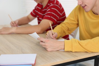 Photo of Students taking exam at wooden table indoors, closeup