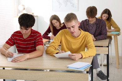 Photo of Students taking exam at wooden table indoors