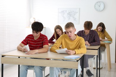Photo of Students taking exam at wooden table indoors