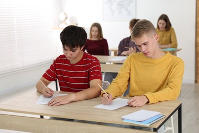 Photo of Students taking exam at wooden table indoors