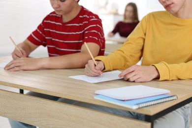 Photo of Students taking exam at wooden table indoors, selective focus