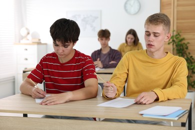 Photo of Students taking exam at wooden table indoors