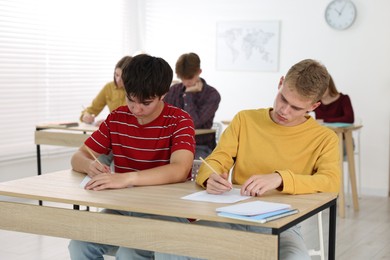 Photo of Students taking exam at wooden table indoors