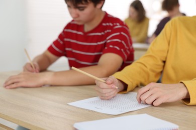 Photo of Students taking exam at wooden table indoors, selective focus