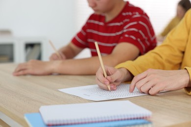 Photo of Students filling out answer sheet at wooden table indoors, closeup. Taking exam