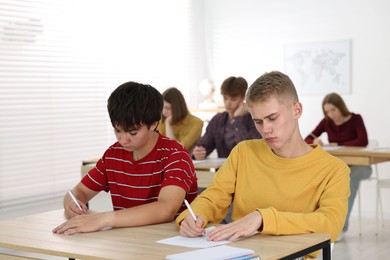 Photo of Students taking exam at wooden table indoors