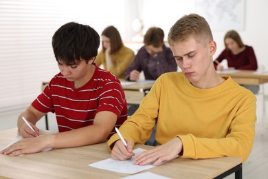 Photo of Students taking exam at wooden table indoors