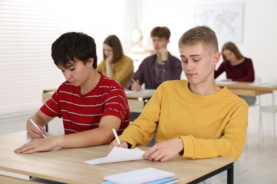 Photo of Students taking exam at wooden table indoors