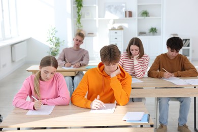 Photo of Students taking exam at wooden table indoors