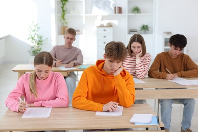 Photo of Students taking exam at wooden table indoors