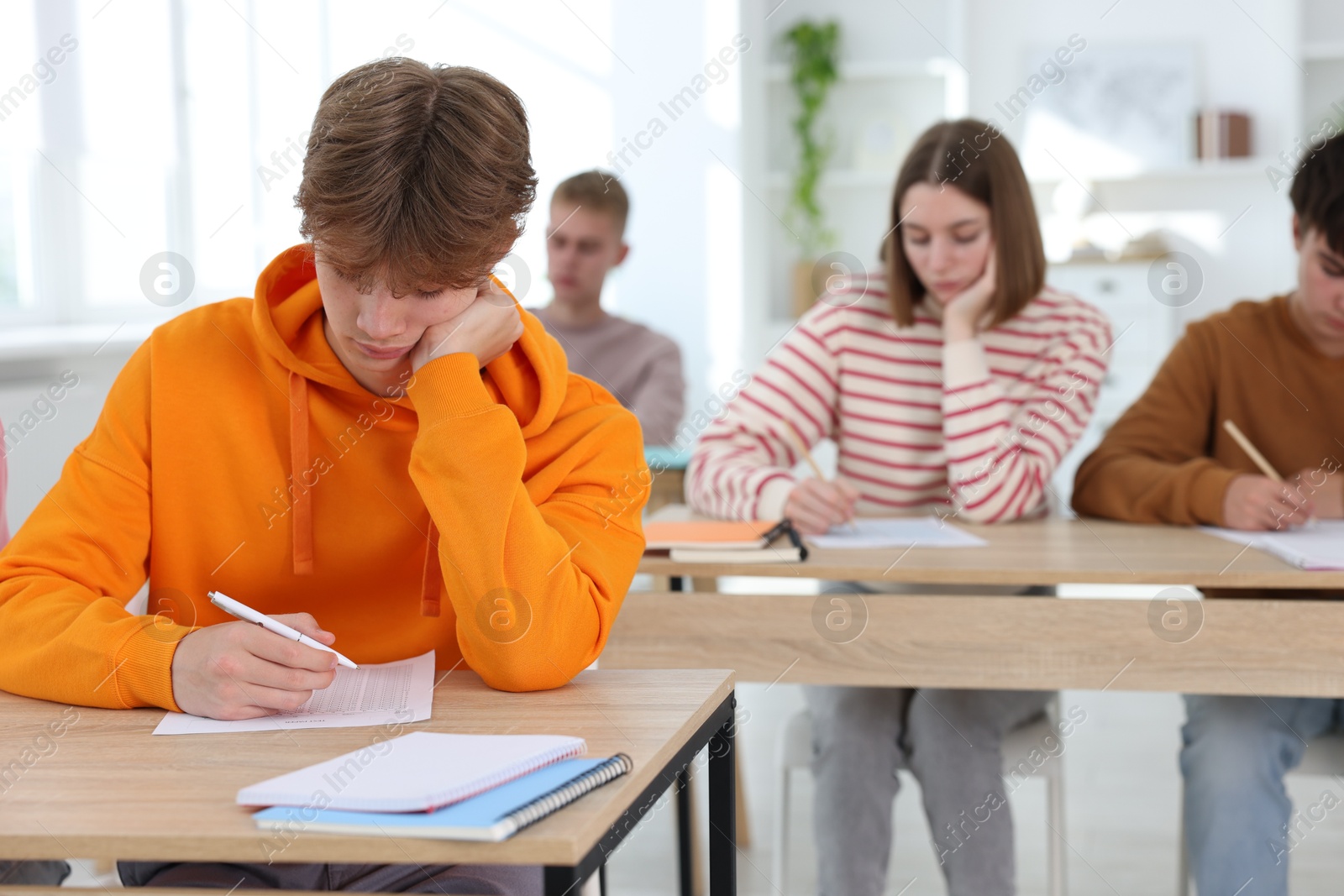 Photo of Students taking exam at wooden table indoors, selective focus