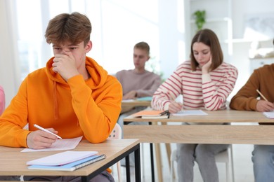 Photo of Students taking exam at wooden table indoors, selective focus