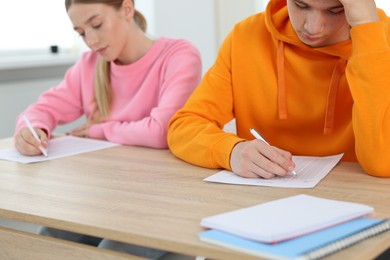 Photo of Students taking exam at wooden table indoors, selective focus