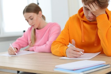 Photo of Students taking exam at wooden table indoors, selective focus