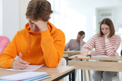 Photo of Students taking exam at wooden table indoors, selective focus
