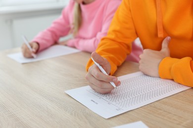 Photo of Students filling out answer sheet at wooden table indoors, closeup. Taking exam