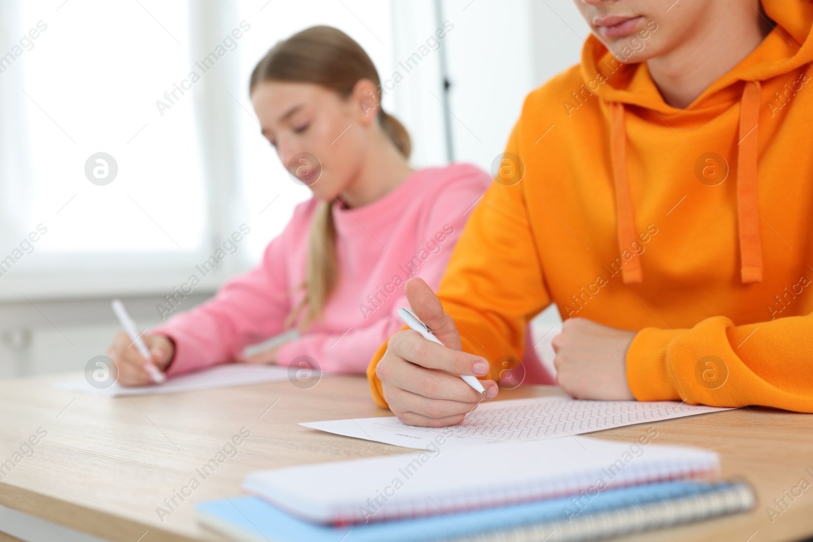 Photo of Students taking exam at wooden table indoors, selective focus