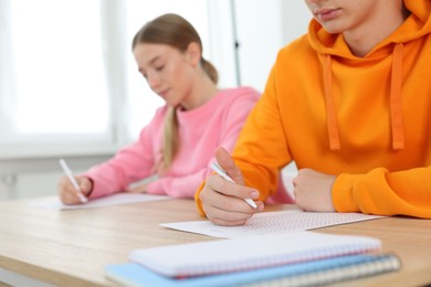 Photo of Students taking exam at wooden table indoors, selective focus