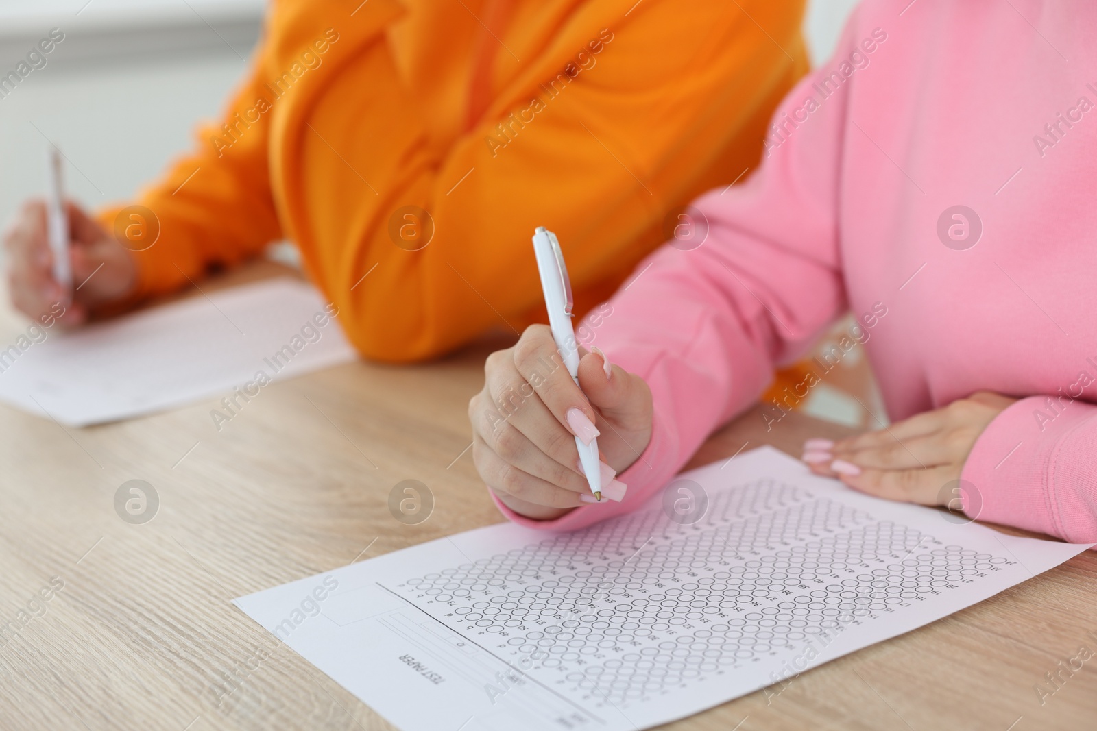 Photo of Students filling out answer sheet at wooden table indoors, closeup. Taking exam