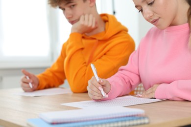 Photo of Students taking exam at wooden table indoors, selective focus