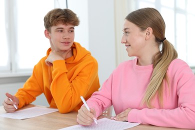 Photo of Students taking exam at wooden table indoors
