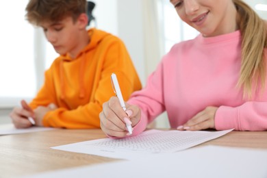 Photo of Students taking exam at wooden table indoors, selective focus