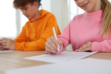 Photo of Students taking exam at wooden table indoors, selective focus
