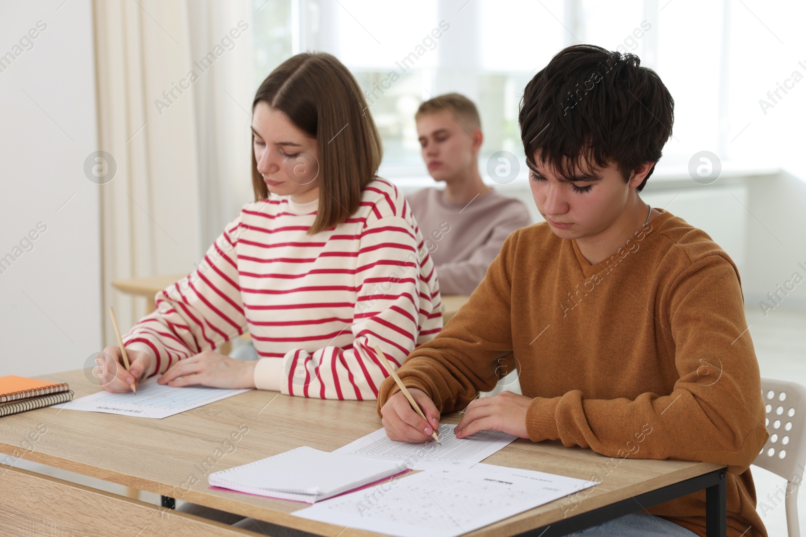 Photo of Students taking exam at wooden table indoors