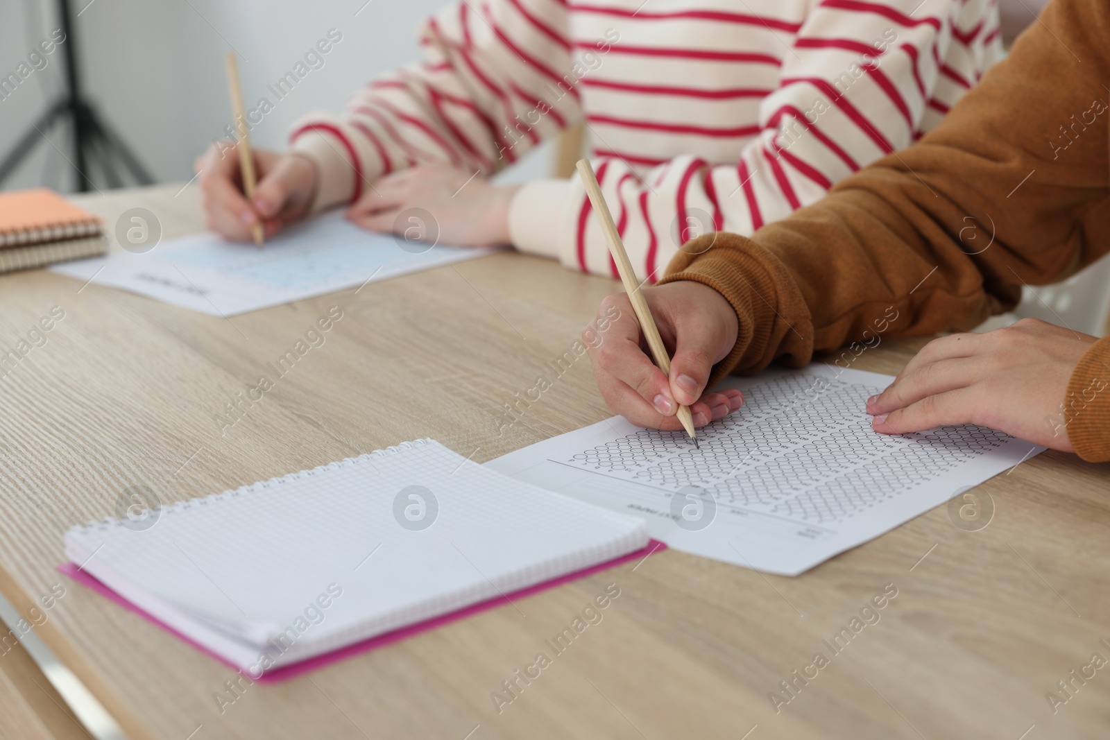 Photo of Students filling out answer sheet at wooden table indoors, closeup. Taking exam