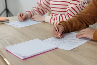 Photo of Students filling out answer sheet at wooden table indoors, closeup. Taking exam