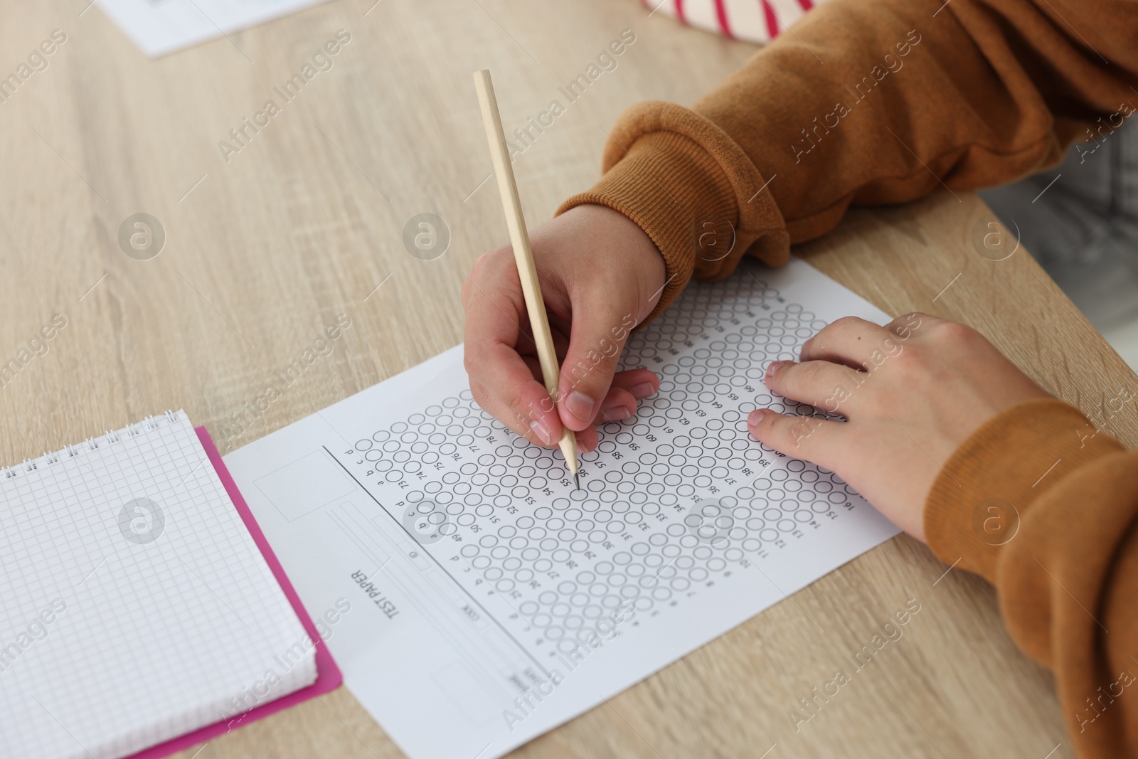 Photo of Student filling out answer sheet at wooden table indoors, closeup. Taking exam