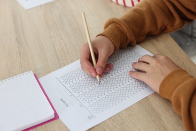 Photo of Student filling out answer sheet at wooden table indoors, closeup. Taking exam