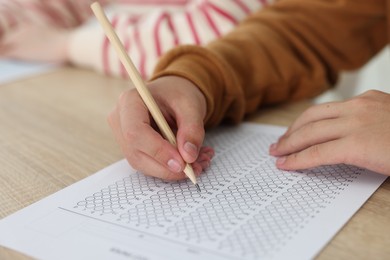 Photo of Students filling out answer sheet at wooden table indoors, closeup. Taking exam