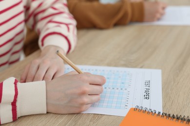 Photo of Students filling out answer sheet at wooden table indoors, closeup. Taking exam