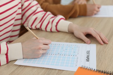Photo of Students filling out answer sheet at wooden table indoors, closeup. Taking exam